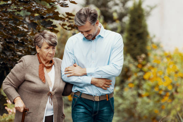 Worried grey senior lady with walking cane in the garden with her son